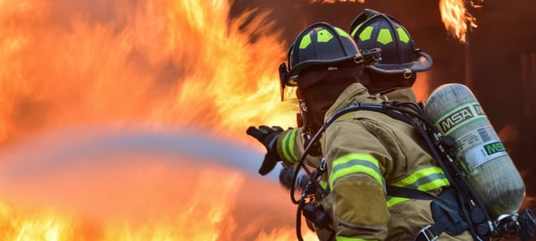 Two firefighter viewed from behind in protective equipment fighting a fire with a water hose