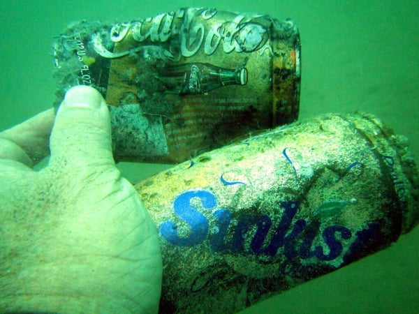 Underwater photo taken by Ghost Net Hunter Harry Chan Tin-Ming 陳天明 holding two aluminium soft drinks cans discarded in the ocean  
