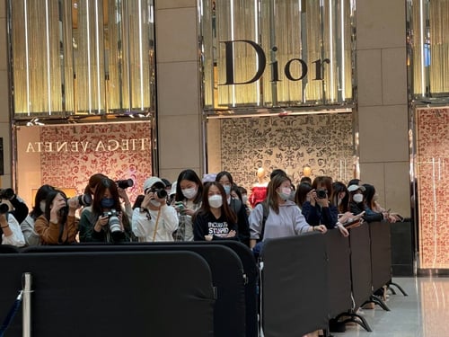 Group of 30 female media photographers wearing masks standing behind a barrier awaiting a celebrity to emerge. Taken at the Landmark Luxury shopping Mall in Hong Kong central. Luxury store Dior with sign in background.  in February 2023 by Guildhawk Evernoon 尚日（香港). Copyright Guildhawk   