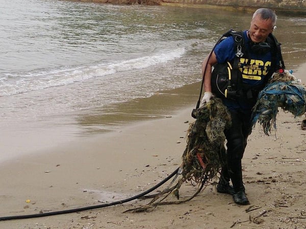 Photograph of Harry Chan the Ghost Net Hunter on a beach in Hong Kong carrying discarded nets he has retrieved from the ocean